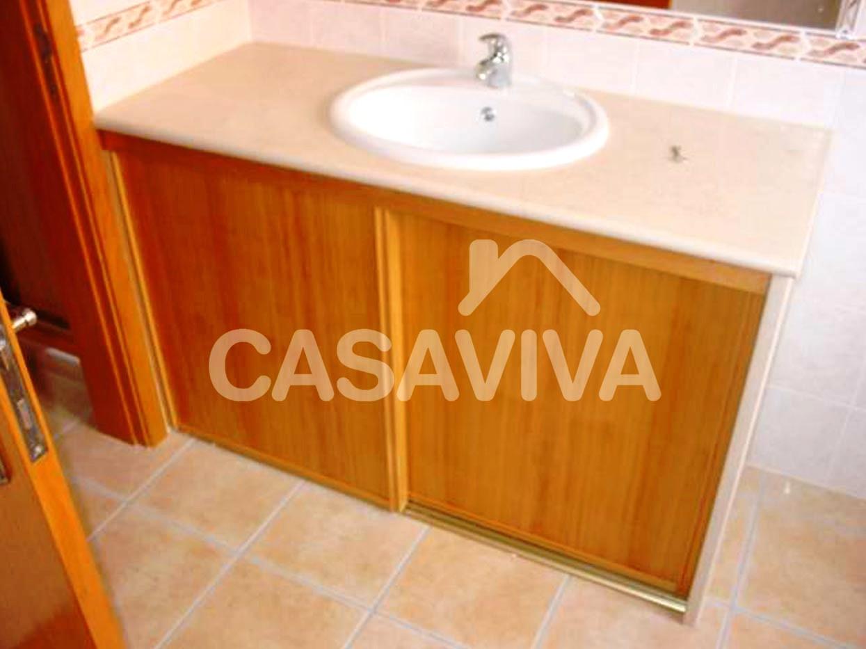 Execuo de mvel de casa de banho com tampo em pedra, lavatrio encastrado, torneira misturadora e portas em madeira.
