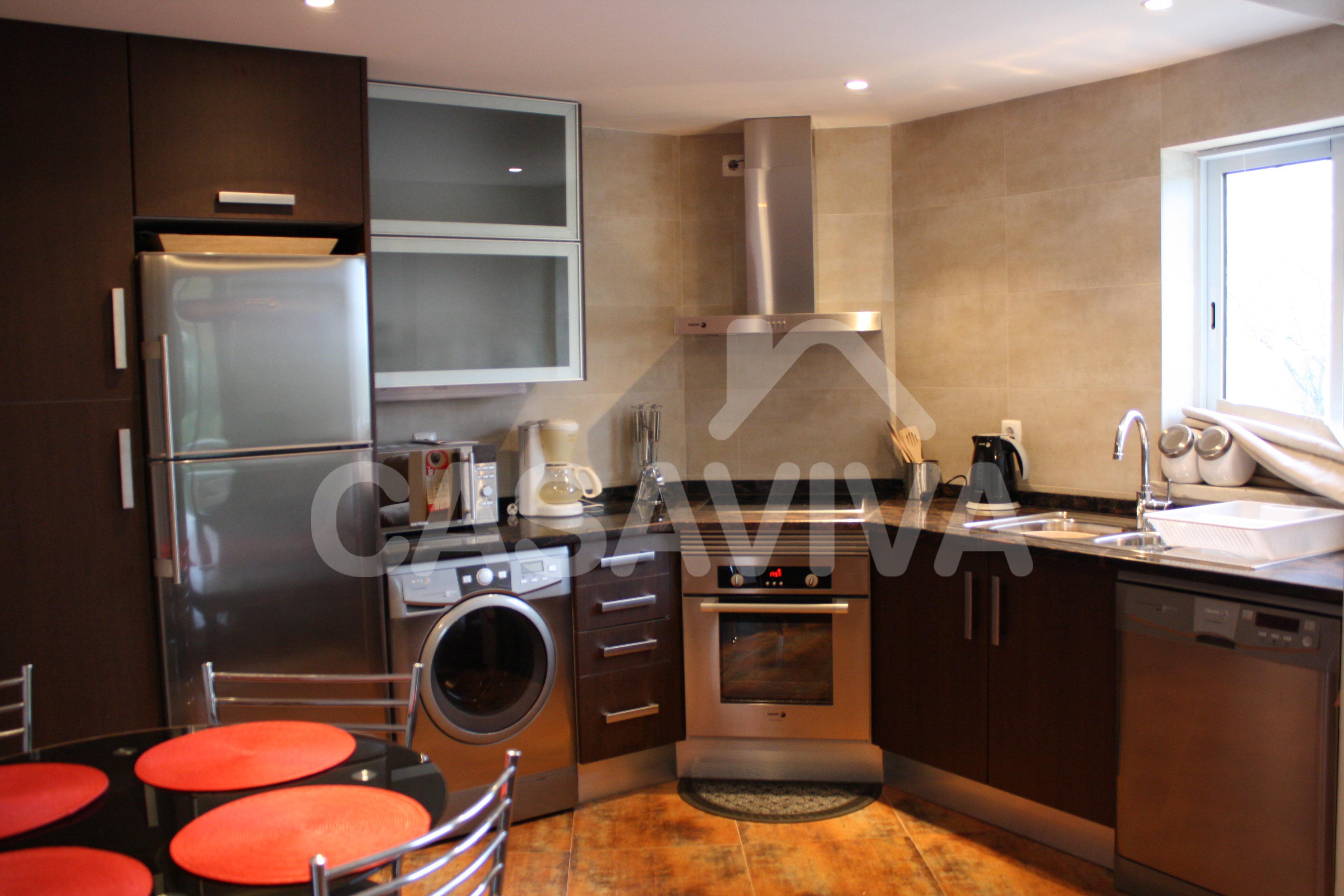 Móveis de cozinha em melamina à medida com electrodomésticos encastrados, exaustor campânula e bancada de pedra com placa de fogão embutida.